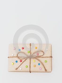 A present or gift box wrapped by rough brown recycled paper and tied with brown hemp rope as ribbon with multi color star isolated