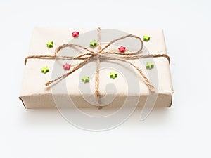A present or gift box wrapped by rough brown recycled paper and tied with brown hemp rope as ribbon with red and green star isola