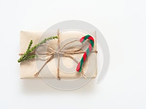 A present or gift box wrapped by rough brown recycled paper and tied with brown hemp rope ribbon with pine branch and candy cane i