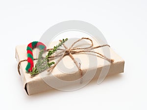 A present or gift box wrapped by rough brown recycled paper and tied with brown hemp rope ribbon with pine branch and candy cane i