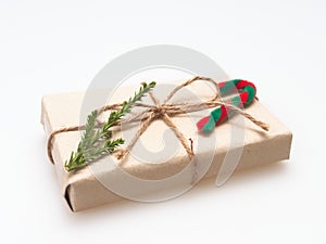 A present or gift box wrapped by rough brown recycled paper and tied with brown hemp rope ribbon with pine branch and candy cane i