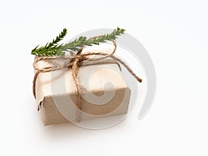 A present or gift box wrapped by rough brown recycled paper and tied with brown hemp rope ribbon with pine branch isolated on whit