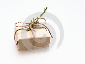 A present or gift box wrapped by rough brown recycled paper and tied with brown hemp rope ribbon with pine branch isolated on whit