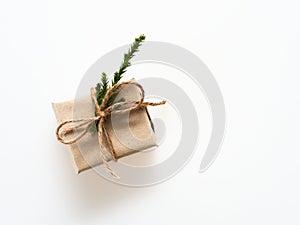 A present or gift box wrapped by rough brown recycled paper and tied with brown hemp rope ribbon with pine branch isolated on whit