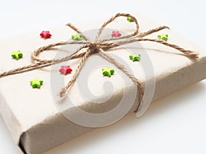 A present or gift box wrapped by rough brown recycled paper and tied with brown hemp rope as ribbon with red and green star isola