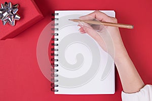 Present and notebook with with new year resolutions list on red background, flat lay style. White page, notebook, plan, write,