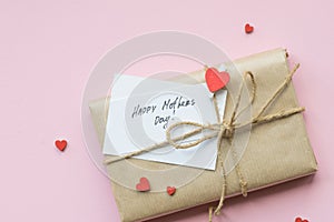 Present wrapped in brown craft paper and tie hemp string on Light pink background. Gift box with greetings on Mothers