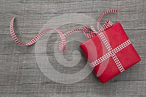 Present wrapped in red paper on a wooden background, checkered ribbon