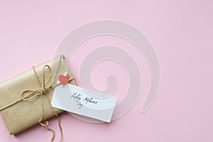 Presents wrapped in brown craft paper and tie hemp string on Light pink background. Gift box with greetings on Mothers