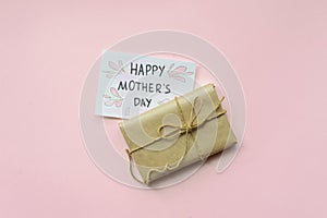 Presents wrapped in brown craft paper and tie hemp string on Light pink background. Gift box with greetings on Mothers Day. Top