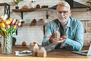 Preservation and restoration of real estate. A mature man holds a model of a house in his hands. Reflects before selling or buying