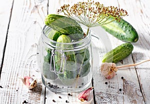 Preserved cucumbers in glass jar with dill and garlic on  table