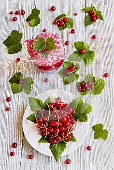 Preserved homemade red currant jam in glass jars on white wooden table. Fresh berries and green leaves, vintage plate, top view