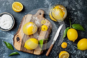 Preserved, salted canned lemons on a wooden board over black stone background. Moroccan cuisine.