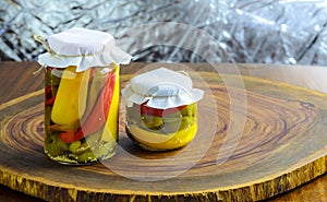 Preserved vegetarian food concept.Canned red, green an yellow peppers in a jar on wooden background