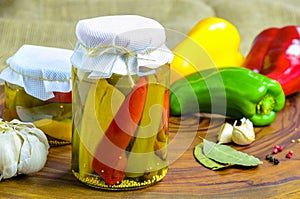 Preserved vegetarian food concept.Canned red, green an yellow peppers in a jar on wooden background