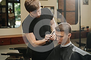 Presision work from hairdresser combing young man`s hair in a barber shop photo