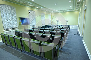 Press briefing room. Seats, monitor, lecterns with microphones set on stage photo