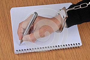 Press freedom concept with someone in handcuffs writing on a spiral notebook with a pen