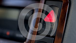 Pressed and glowing emergency car hazard warning flasher button on dashboard