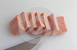 Pressed pork canned meat chunks on a cutting board with knife.