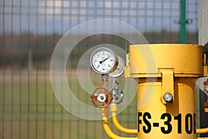 Pressure gauge for measuring the pressure of natural gas in a gas pipeline. Yellow transport pipes on the surface of the fence.