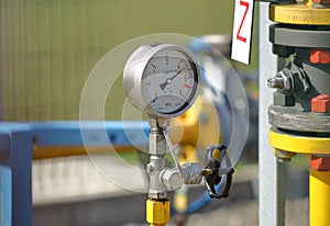 Pressure gauge for measuring the pressure of natural gas in a gas pipeline. Yellow transport pipes on the surface of the fence.