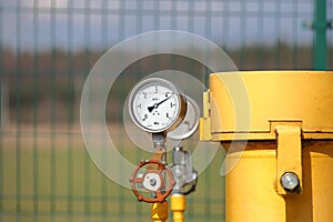 Pressure gauge for measuring the pressure of natural gas in a gas pipeline. Yellow transport pipes on the surface of the fence.