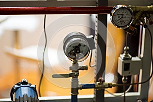 Pressure gauge psi meter in pipe and valves of water system industrial focus left closeup white light defocus blur background