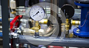 Pressure gauge psi meter in pipe and valves of water system industrial focus left closeup white light defocus blur background