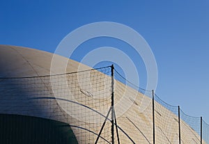 A pressure switch structure with a plastic cover of a sports building surrounded by a metallic fence (Pesaro)