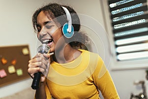 Preteen black girl holding microphon singing karaoke at home, recording songs for contest. Children's lifestyle concept