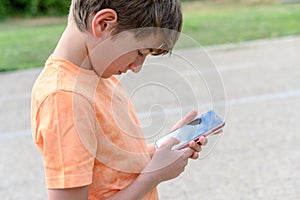Preteen boy entertains himself by looking at his mobile phone in the street. Concept of addiction to technologies