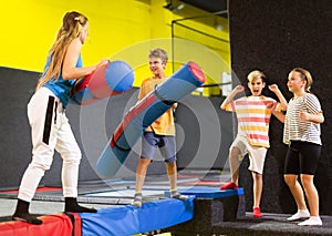 Preteen boy fighting by inflatable pugil sticks with girl