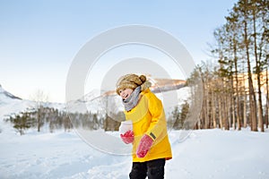 Preteen boy having fun playing with ice or snowball in forest among mountain valley on sunny day.
