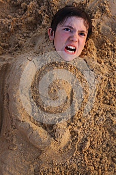 Preteen boy head in the beach sand happy smiling