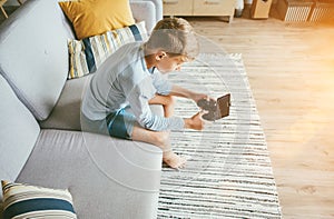 Preteen boy losted in computer game. Sits at home on coze sofa, uses gamepad with smartphone photo