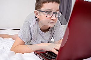 A preteen boy lying on a bed, surfing internet and typing into his blog, child blogging concept