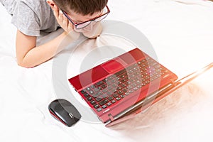 A preteen boy lying on a bed, surfing internet and typing into his blog, child blogging concept