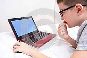A preteen boy lying on a bed, surfing internet and typing into his blog, child blogging concept