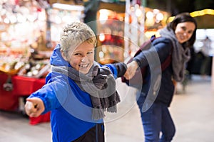 Preteen boy pulling mom hand at outdoor Christmas market