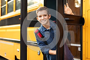 Preteen boy standing in door of school bus and looking at camera