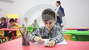 Preteen boy studying in classroom on background with classmates and teacher