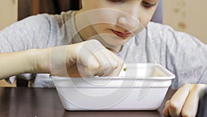 A preteen caucasian boy eating chineese fast food, instant noodles from disposable container at home, his mouth is dirty