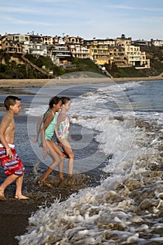 Preteen children playing at the beach running into waves