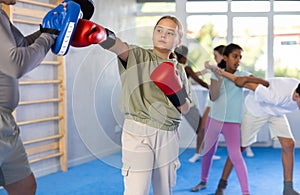 Preteen girl in boxing gloves practicing punches on mitts with coach