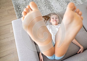 Preteen girl lying on couch with her bare feet raising up high photo