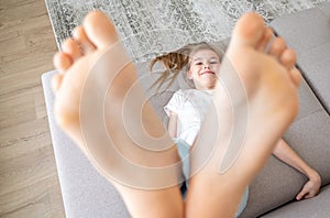 Preteen girl lying on couch with her bare feet raising up high