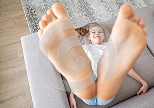 Preteen girl lying on couch with her bare feet raising up high