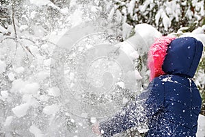 Preteen girl in pink warm hood shakes the snow from a branch outside on nature winter snowy forest background. Avalanche